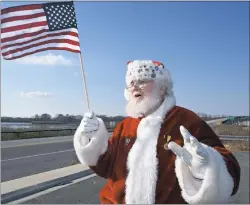  ?? PHOTO BY TOM MCCALL ?? Only in America are you likely to see a patriotic flag-waving Santa. He set up his post on the Caroline County side of the Dover Bridge. The Choptank River rolled by as honking trucks and cars made their approval known.
