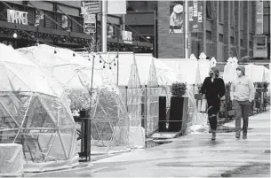  ?? NAM Y. HUH AP ?? People walk by outdoor plastic dining bubbles on Fulton Market in Chicago.