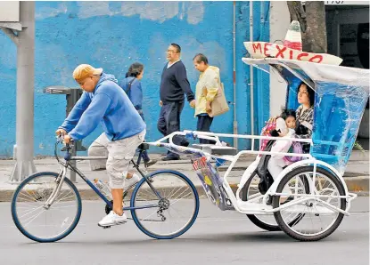  ??  ?? El conductor de un bicitaxi transporta a madre e hija por calles de CdMx.