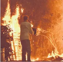  ?? PHOTO: REUTERS ?? Futile . . . A resident pours a bucket of water trying to douse flames caused by the Woolsey Fire in Malibu, California, on Saturday.