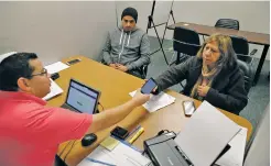  ?? LM OTERO/THE ASSOCIATED PRESS ?? Community Council health care navigator Fidel Castro Hernandez, left, hands a Spanish help line phone to legal U.S. resident Maria Ana Pina, right, in December as she signs up for the Affordable Care Act with her son Roberto Pina at the Community...