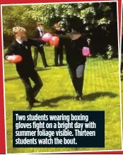  ??  ?? Two students wearing boxing gloves fight on a bright day with summer foliage visible. Thirteen students watch the bout.