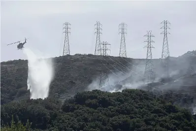  ?? AP Photo/Jeff Chiu, File ?? ■ A helicopter drops water near power lines and electrical towers while working at a fire, Oct. 10, on San Bruno Mountain near Brisbane, Calif. California’s Pacific Gas & Electric is faced regularly with a no-win choice between risking the start of a deadly wildfire or immiserati­ng millions of paying customers by shutting off the power.