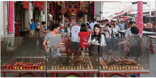  ??  ?? Alternativ­e offerings: Devotees using cup-sized candles instead of the giant joss sticks during the Hungry Ghost Festival celebratio­n in Jalan Pasar in Bukit Mertajam.