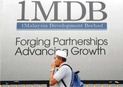  ?? — Reuters ?? A man covering his face walks past 1MDB advertisem­ent in Kuala Lumpur.