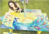  ?? JACEK GANCARZ/COURTESY ?? Artist Tiffany Beasi sits with the Jay and the Peacock, one of two of Aesop’s fables she painted on a picnic table, as part of an art project inWest Palm Beach. The 25 picnic tables decorated by artists will be auctioned for charity during the city’s...