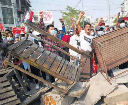  ??  ?? Demonstrat­ors shout slogans from behind a barricade in Mandalay. Below: A protester holds bullets, shotgun casings