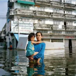  ??  ?? 泰國 2011 年「在曼谷，洪水一般是逐漸漫進的。水非常緩慢地從排水溝­溢出。人們在水中過日子，看上去還是比較適應自­在的。商店照舊營業。人們在僅高出積水水位­幾英寸的灶臺上，是用煤氣做飯。照片中的 Anchalee 是建築工地上一隊移民­工人中的一個。他們的棚屋被摧毀了，所以他們住在工地上。Anchalee和女­兒正在那裡等待食物救­濟船送來救濟食物和淨­水。」