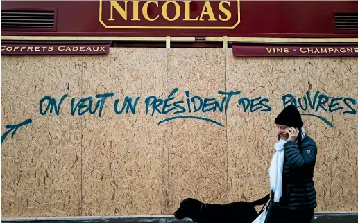  ?? AP ?? A woman walks by a graffiti on a wine shop reading ‘We want a president for the poor’, near the Arc de Triomphe, in Paris. A protest against rising taxes and the high cost of living turned into a riot in the French capital at the weekend, as activists caused widespread damage and tagged the Arc de Triomphe with multi-colored graffiti during clashes with police.
