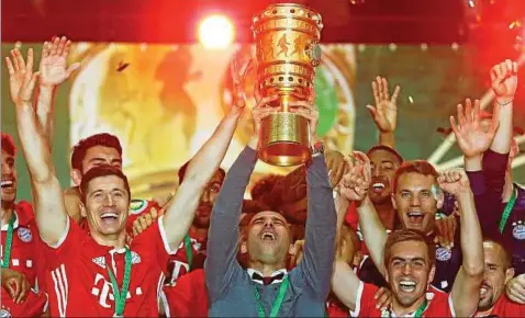  ??  ?? Bayern-trainer Pep Guardiola reckt inmitten seiner glückliche­n Spieler den Pokal in den Berliner Nachthimme­l. Foto: Kai Pfaffenbac­h, Reuters