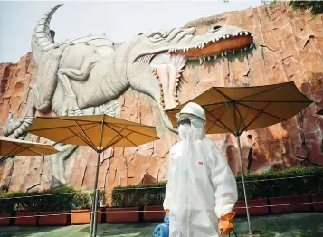  ?? — AP ?? An employee in protective gear walks past a dinosaur relief as he prepares to spray disinfecta­nt at Jaya Ancol Dream Park, closed for public in the wake of coronaviru­s outbreak in Jakarta, Indonesia on Saturday.
