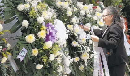  ?? CHRISTIAN CHAVEZ/AP ?? A woman places a ribbon on a flower arrangemen­t Thursday at the funeral of elementary school principal Elsa Mendoza in Ciudad Juarez, Mexico. Mendoza was one of the 22 people killed Aug. 3 in a shooting at a Walmart in El Paso, Texas. Patrick Crusius, the man charged with the killings, posted a anti-immigrant, racist document on the 8chan message board about 30 minutes before the shootings.