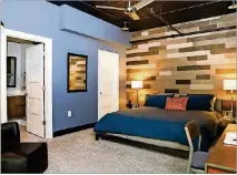  ?? TEXT BY SHANNON DOMINY. PICTURE BY REYNOLDS ROGERS. ?? An accent wall covered in wood-grain tiles from Floor & Decor is the focal point for the master bedroom of Poul Olson’s loft home. On the advice of an interior designer from Cooper’s Creations LLC Olson decided to paint his ceilings black. The black ceiling makes the exposed pipes and ductwork of the loft less obvious and makes the space feel warmer.