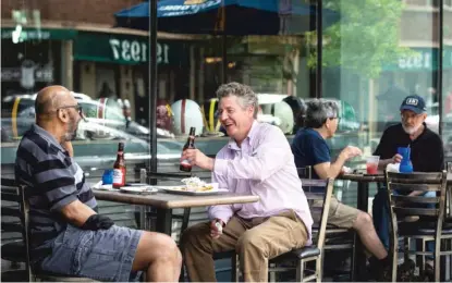  ??  ?? Bill Luby (center), 54, laughs with his friend, Calvin Grant, 53, both from Evanston, as they eat and drink on the patio at Bluestone, 1932 Central St. in Evanston, in May.