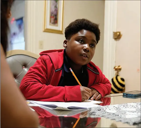  ?? STEVEN SENNE / ASSOCIATED PRESS (2022) ?? J. Ryan Mathurin does his homework as his mother, Evena Joseph, watches at their Boston home.