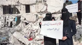  ?? HUSSEIN MALLA/AP ?? Women stand in the rubble with placards reading “United Nations are the partners of Bashar Assad and killing Syrians,” in Atareb, Syria.