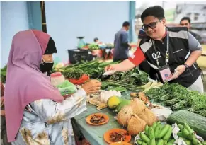  ?? ?? Meet and greet: Mohd nor Izzat distributi­ng pamphlets and introducin­g himself to the voters at the wet market in Tanjung Malim.