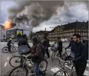  ?? EMIL NICOLAI HELMS — RITZAU SCANPIX VIA AP ?? People ride bicycles as smoke rises from the Old Stock Exchange in Copenhagen, Denmark, Tuesday.