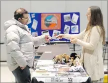  ?? Colleen De Neve, Calgary Herald ?? Lauren Shanahan of Roots and Shoots at the University of Calgary hands Ahmed Shalaby a brochure during a philanthro­py fair.