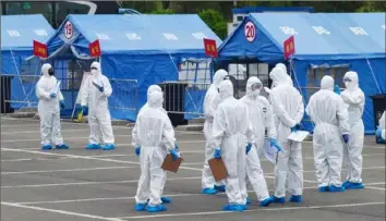  ?? Associated Press ?? Government workers outside a blue tent used to coordinate transporta­tion of travelers from Wuhan to designated quarantine sites in Beijing on April 15, 2020.