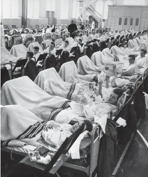  ?? The Associated Press ?? ■ Danish personnel suffering from influenza occupy beds in temporary sick quarters set up in a gymnasium at Copenhagen’s naval shipyard to handle the large number of patients on Oct. 12, 1957.