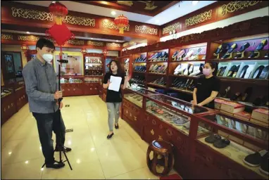  ?? ASSOCIATED PRESS ?? In this April 28 photo, Cheng Xu (center) shows her footwear for her online clients through the live-streaming at the Neilianshe­ng Footwear in Beijing