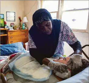  ?? Cloe Poisson / C-HIT.org ?? Dilliner Jordan wipes Tracy Lamb’s face while caring for her in Lamb’s West Haven apartment on March 22. Jordan is a home health care worker who cares for Lamb four days a week.