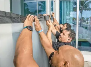  ?? WILLIE J. ALLEN JR./ORLANDO SENTINEL ?? Wyndham Grand Clearwater Beach workers tape up the top of the glass door facing the beach as they prepare for Hurricane Ian’s arrival in Clearwater on Tuesday.