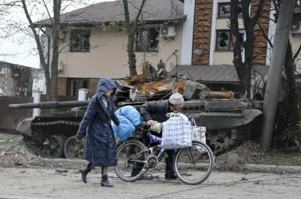  ?? Alexei Alexandrov, The Associated Press ?? Residents of Mariupol, Ukraine, walk past a tank destroyed during heavy fighting in an area controlled by Russian-backed separatist forces on Tuesday. According to a poll, many Americans question whether the U.S. is doing enough in response to Russia’s invasion of Ukraine, although few want U.S. troops to get involved.