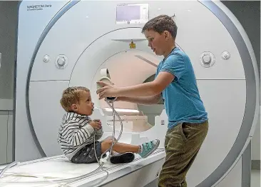  ?? WARWICK SMITH/ STUFF ?? Harrison Atkins, 2, sitting on the MRI scanner at Pacific Radiology in Palmerston North, with Cam Mackintosh, 10, who helps Harrison to get acquainted with the equipment.