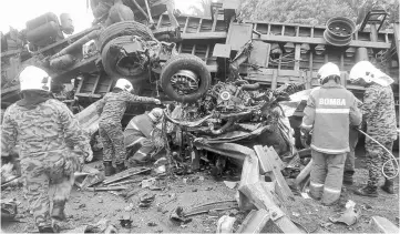  ??  ?? Fire and Rescue personnel inspect the crushed MPV at the scene of the accident. — Bernama photo