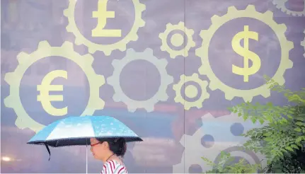  ?? AP ?? In this July 20, 2018 photo, a woman carries an umbrella as she walks past a mural displaying world currency symbols outside a bank in Beijing.