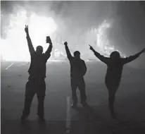  ?? Associated Press file photo ?? People watch as stores burn on Nov. 25, 2014, in Ferguson, Mo. The four Republican candidates in Missouri’s gubernator­ial primary on Aug. 2 are pledging an aggressive law-and-order approach, two years after the fatal Ferguson police shooting of Michael...