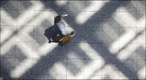  ?? AP ?? In this file photo, a businessma­n walks on the floor where lies the shadow cast by the glass roof of a building in Tokyo. The Japan Meteorolog­ical Agency has announced that the rainy season in Kanto area appeared to be over in August.