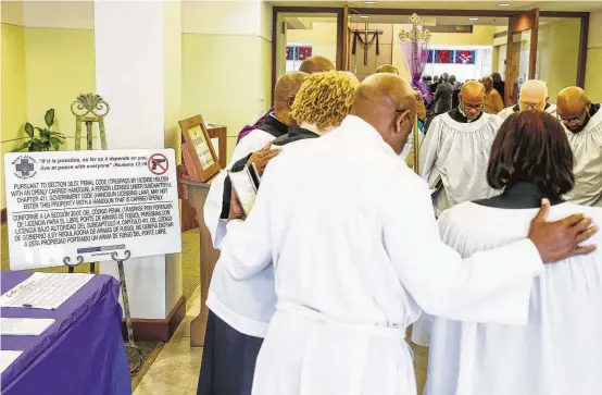  ?? Michael Ciaglo / Houston Chronicle ?? St. James Episcopal Church choir members pray near signage stating the church’s gun policy.