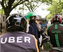  ?? — Reuters ?? A passenger of Grab bike fixes her helmet next to Uber driver at Manggarai train station in Jakarta, Indonesia.