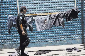  ?? SILVIA IZQUIERDO/THE ASSOCIATED PRESS ?? A police officer walks next to uniforms painted with red ink to symbolize blood during a protest Friday in Rio de Janeiro. A weeklong strike involving members of the military police has paralyzed the southeaste­rn Brazilian state of Espirito Santo.