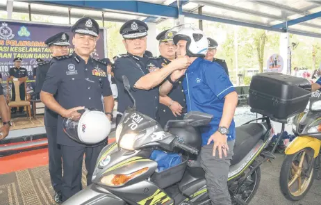  ?? — Photo by Chimon Upon ?? Mancha, flanked by Ibrahim (left) and Norizan, helps a motorcycli­st put on a helmet during the launch of the Chinese New Year Ops Selamat campaign.