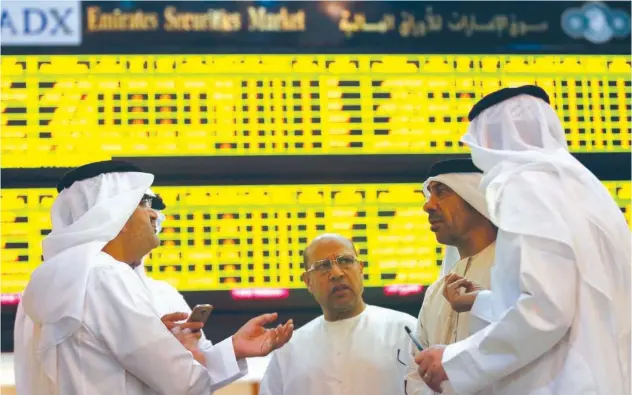  ?? ?? ↑
Investors speak in front of a screen displaying stock informatio­n at the Abu Dhabi Securities Exchange.