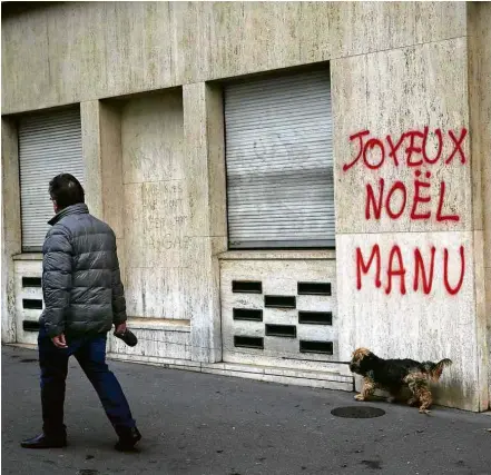  ?? Christophe Ena/Associated Press ?? Homem passa com cão diante de pichação ‘Feliz Natal, Manu’, alusão ao presidente Emmanuel Macron
