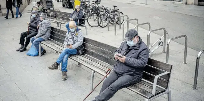  ?? Manu Mitru ?? Dos jubilats consulten el mòbil en un banc, a Barcelona.