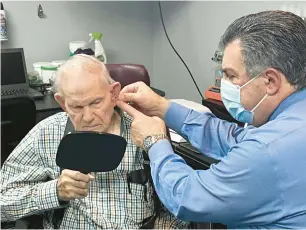  ?? ?? Moseley watches Dr. Peter Sotiropoul­os demonstrat­e how to put in his new hearing aid this month in Steger. Moseley, a regular on area dance floors, had stopped coming out after his old hearing aid stopped working.