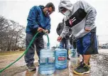  ?? Brett Coomer / Staff photograph­er ?? Victor Hernandez, left, and Luis Martinez fill their water containers with a hose from a spigot Feb. 2 in Haden Park as the freeze left many without water.