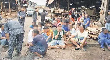  ??  ?? Illegal immigrants rounded up and waiting to be questioned by immigratio­n officers at a sawmill in Bintulu recently.