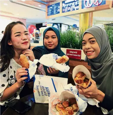  ?? — IBRAHIM MOHTAR/ The Star ?? No issue here: Three Auntie Anne’s customers enjoying their pretzel dogs at an outlet in Kuala Lumpur.