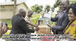  ??  ?? Councillor Phiri in a black jacket hands over exercise books and cleaning materials to Lilayi Primary school