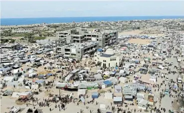  ?? /Reuters ?? Hellish: People walk near tent camps where displaced Palestinia­ns take shelter in Rafah near the Egyptian border. Outbreaks of epidemics of diseases is being predicted by UN officials.