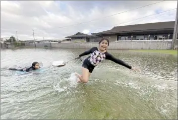  ?? The Maui News / COLLEEN UECHI photo ?? Hawaiian Mission Academy Maui students Natalie Luwalhati (left) and Marley Baker play in the flooded yard fronting their school in Kahului on Saturday afternoon. Record rainfall in the area turned places like the schoolyard and the adjacent parking lot of the Kahului Seventh-day Adventist Church into a shallow lake.