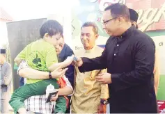  ??  ?? Nizam (second right) presenting Hari Raya aid to an autistic child on Saturday.