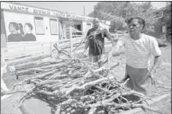  ??  ?? Volunteers Ron Hicks (left) and Magnolia Scullark pile debris into a wheelbarro­w in front of the center where a newly constructe­d outdoor deck and handicap ramp were damaged.